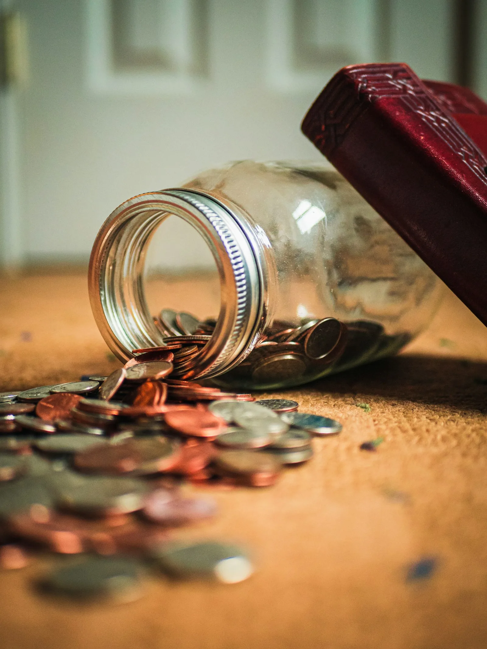 Photo of a glass jar overturned, with bunch of coins in it.
