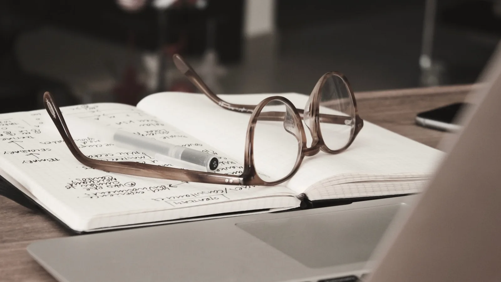 Image of a diary with lots of research notes in it along with a spectacle and a pen