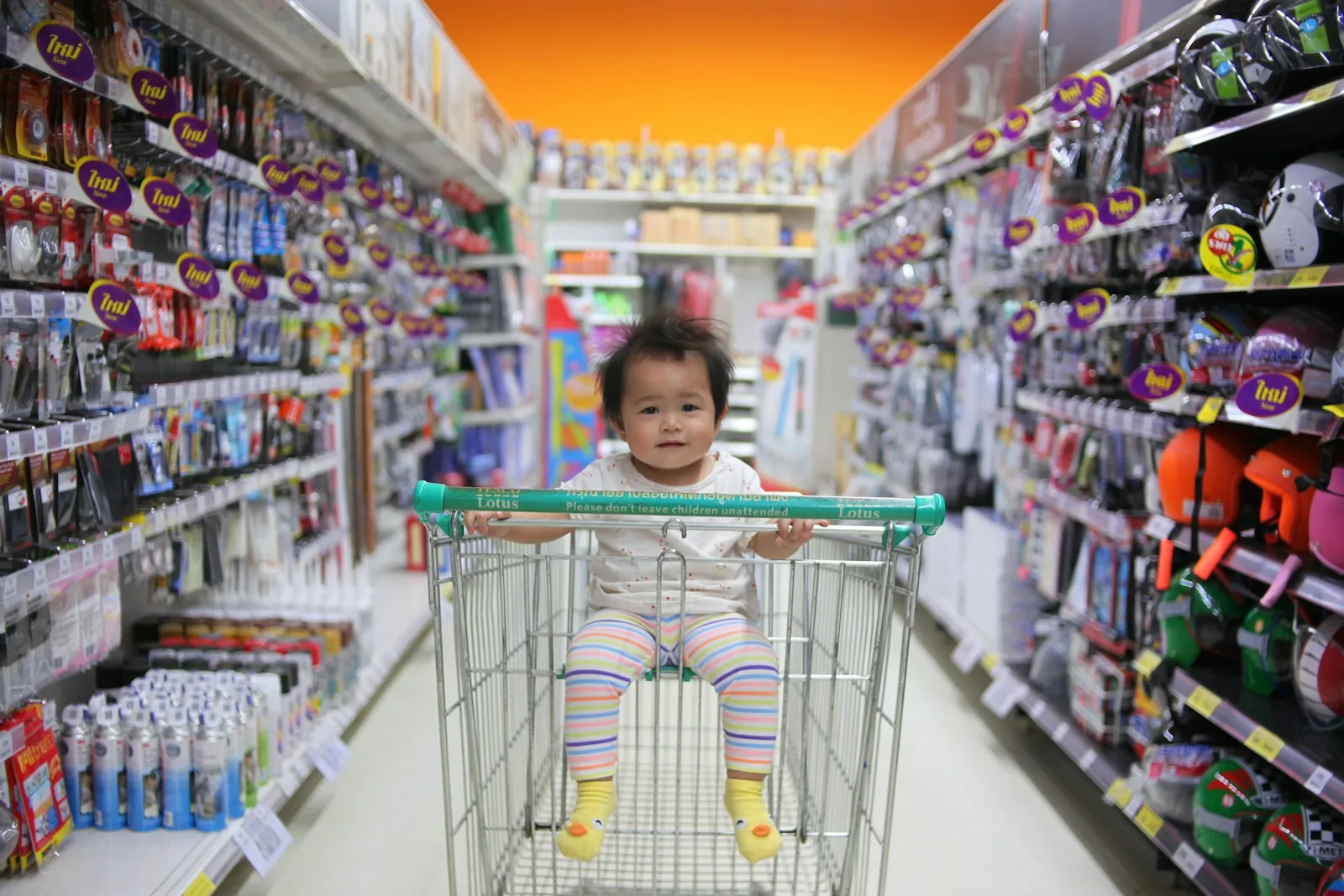 A kid sitting in a supermarket trolley