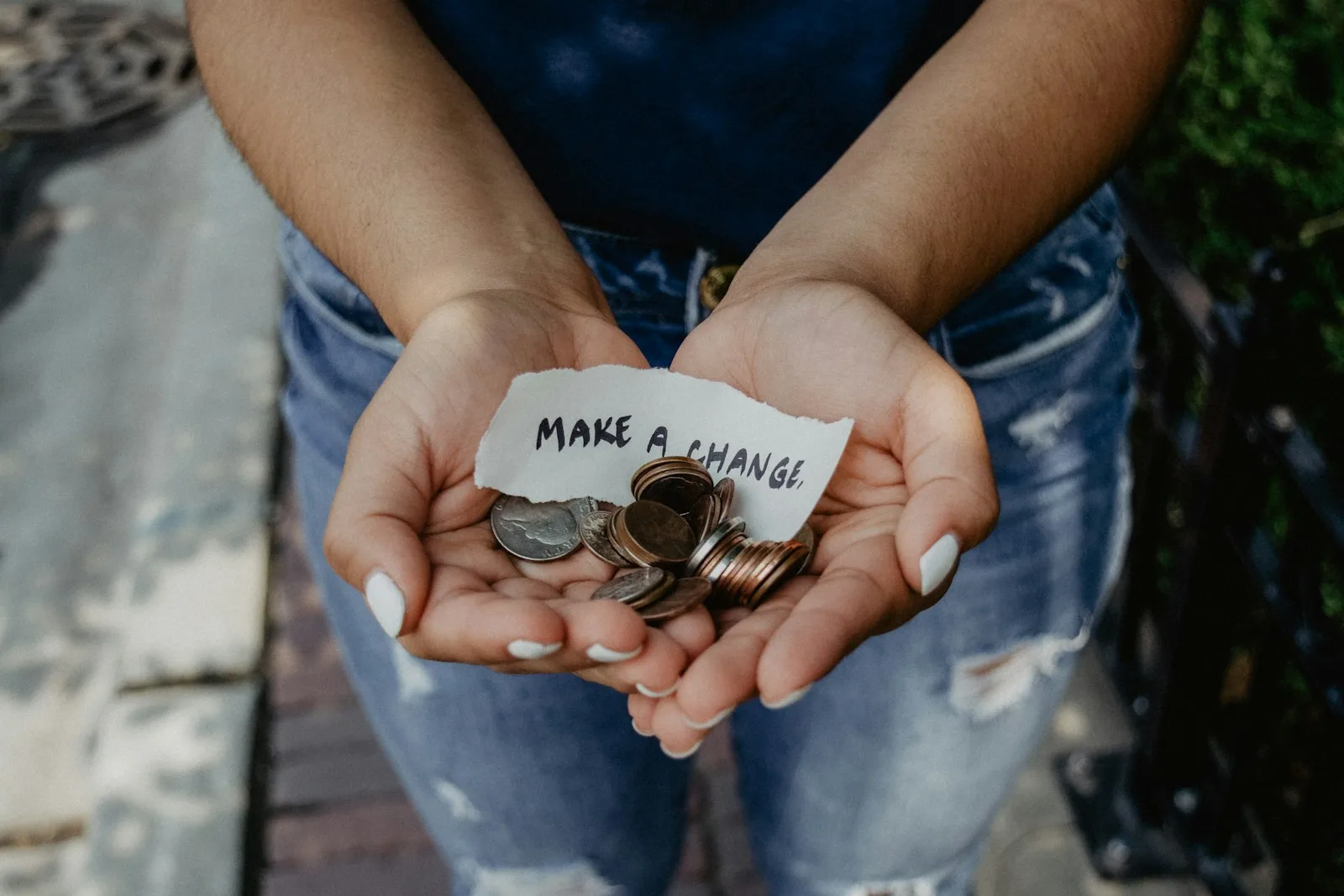 A person holding out coins with a paper on it saying “Make a Change”
