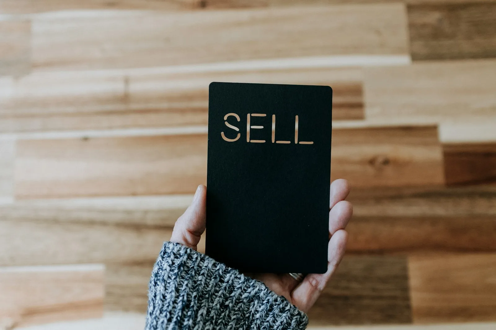 Image of a person holding a paper with the word “SELL” written on it