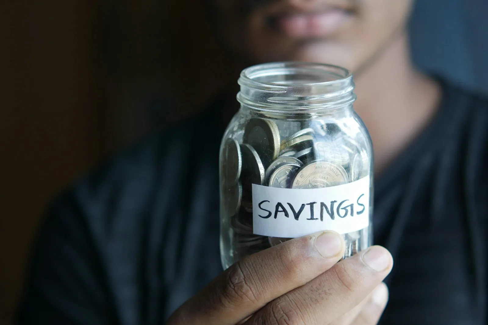 A person holding up a bunch of coins in a jar with the label of “Savings”